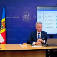 Tomasz Trojan, naczelnik, podczas prezentacji w imieniu Departamentu Usług Cyfrowych. Siedzi przy biurku, przed którym stoją flagi Mołdawii i Polski. Za nim znajduje się niebieskie tło z napisem 'MINISTERUL ENERGIEI REPUBLICII MOLDOVA' oraz herbem Ministerstwa Energii Mołdawii. Po jego prawej stronie widoczny jest duży ekran z wyświetlonym systemem poczty elektronicznej lub zarządzania dokumentami. 