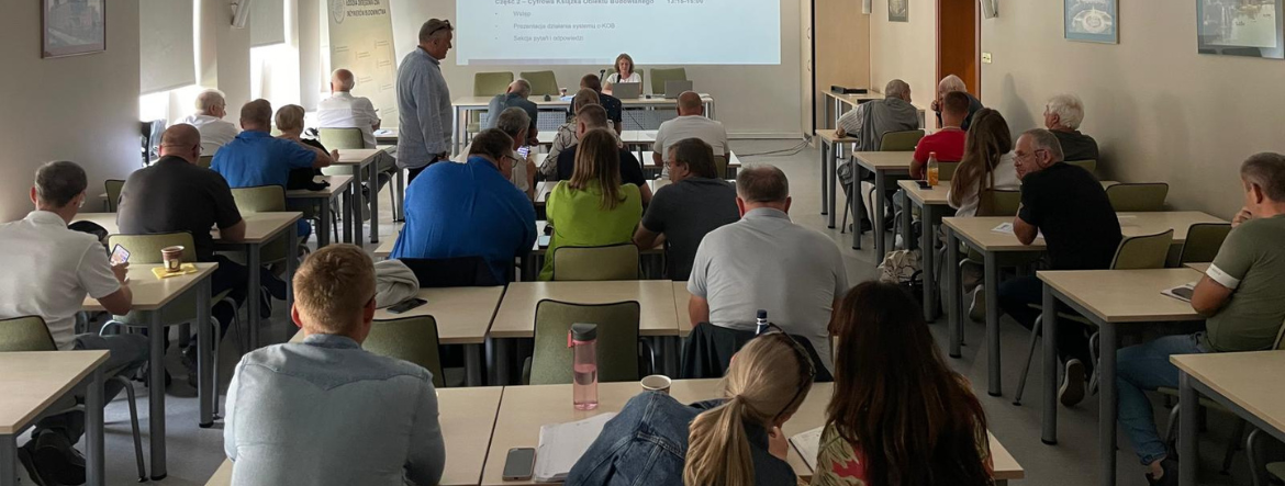 Na zdjęciu sala szkoleniowa – uczestnicy siedzą przy stołach, słuchają prelegenta, na ekranie widoczny jest slajd z planem szkolenia dotyczącym Elektronicznego Dziennika Budowy i Cyfrowej Książki Obiektu Budowlanego.