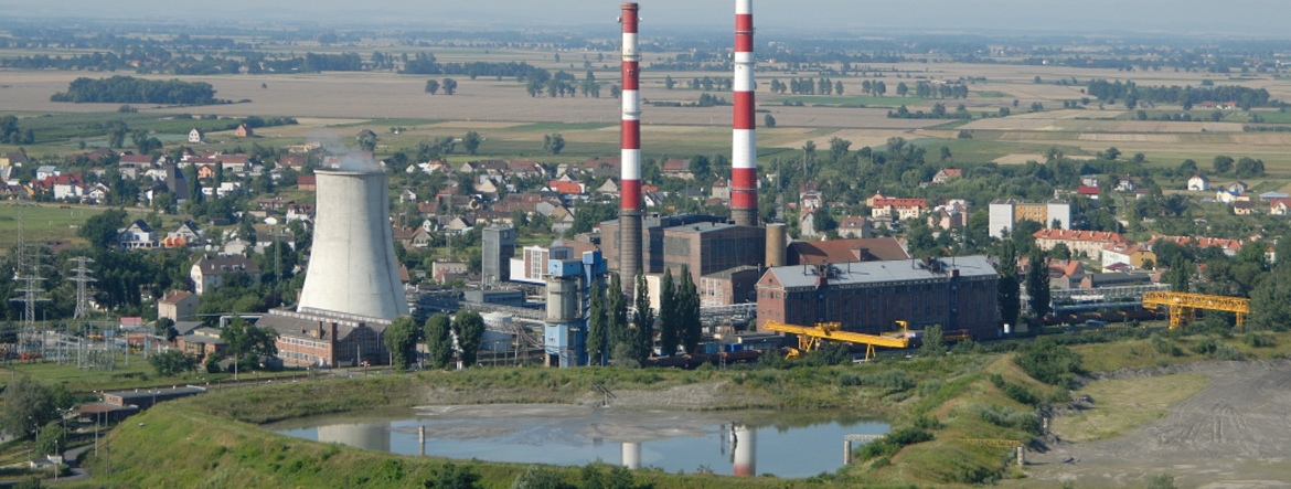 Na zdjęciu widać z lotu ptaka elektrociepłownię kominy, budynki, zbiornik wodny. W pobliżu znajdują się pola i budynki mieszkalne.